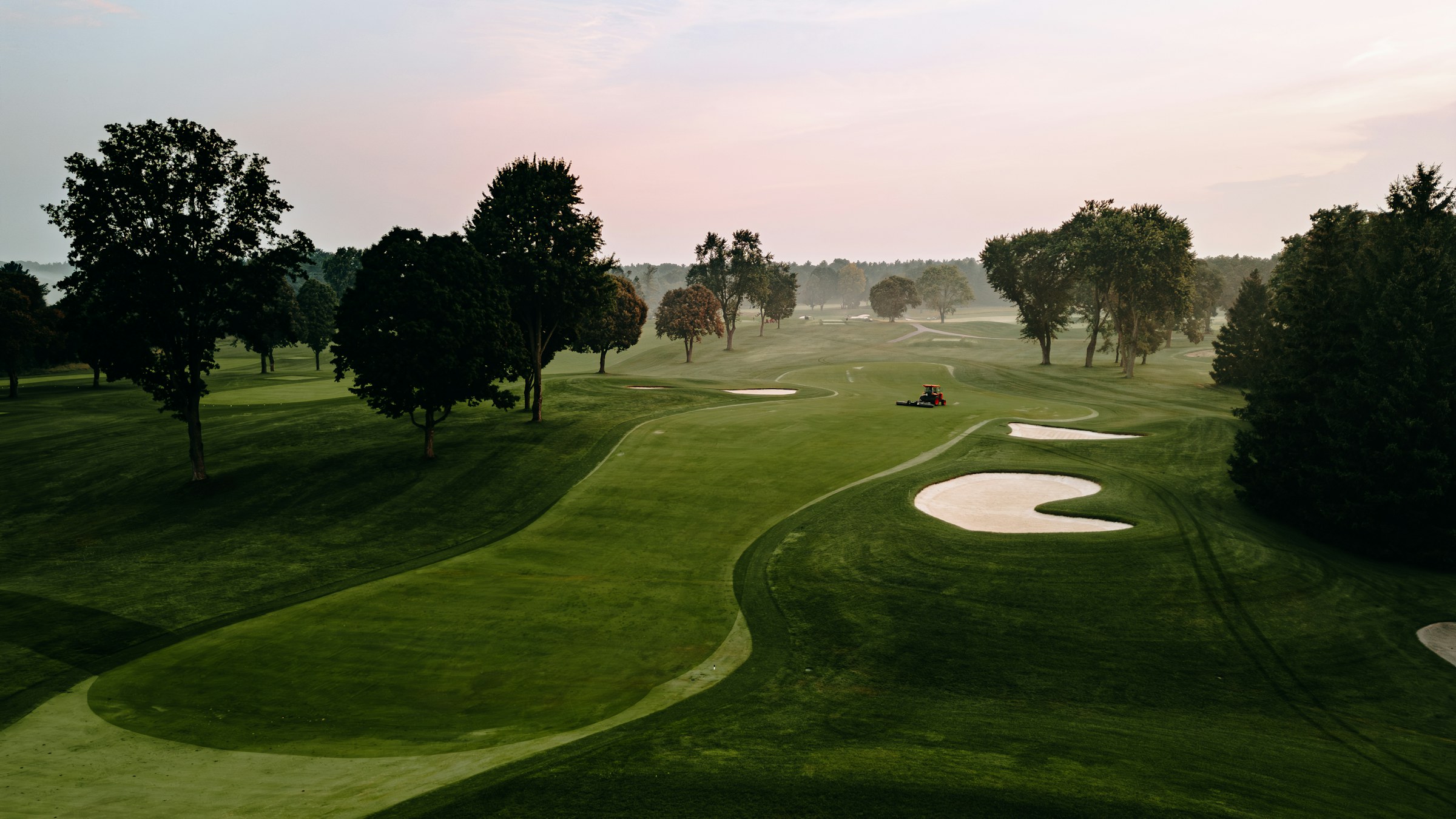 Le fairway rectiligne du trou 2 bordé d'arbres, bunker de droite en vue