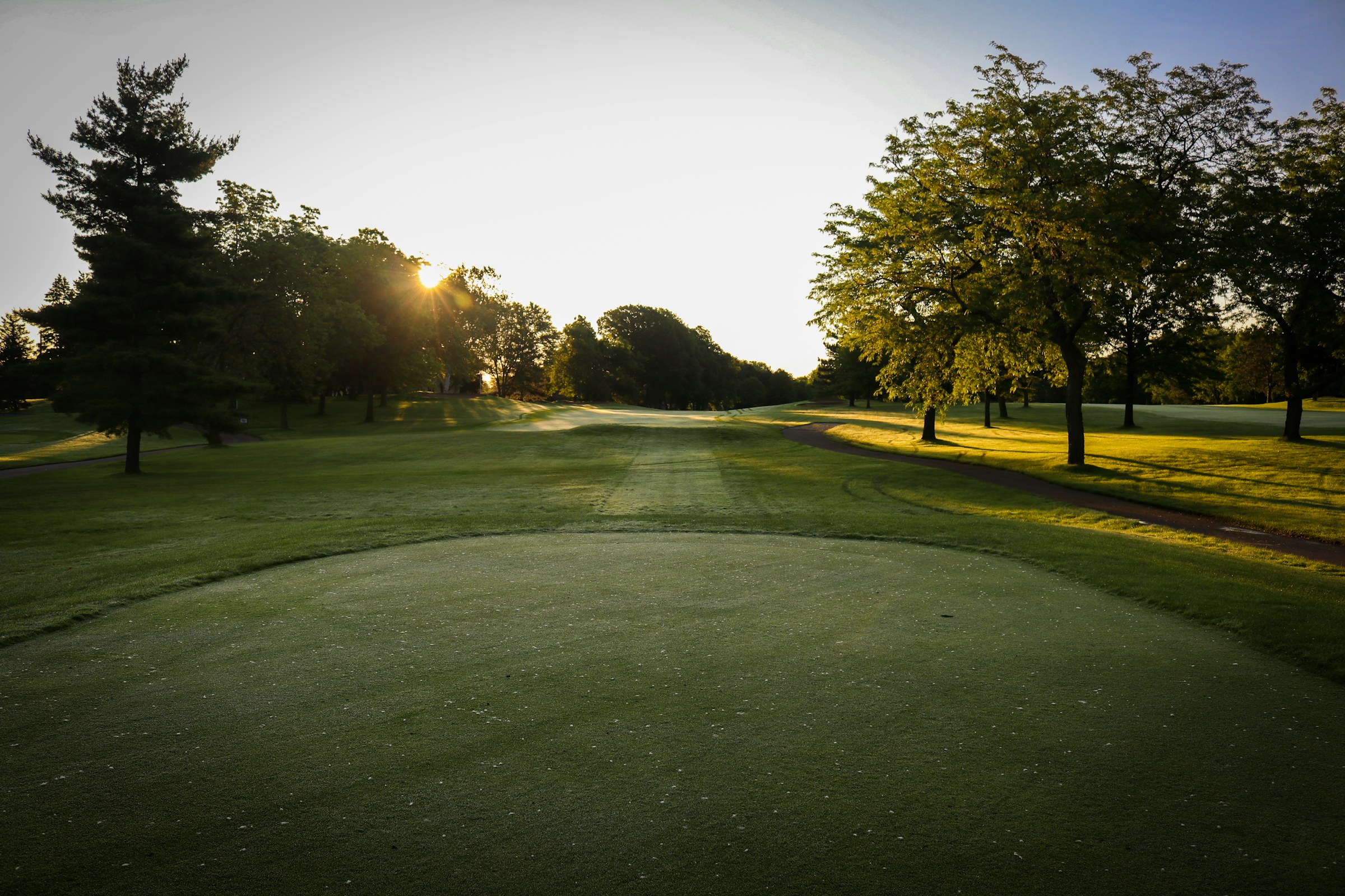 Le fairway du trou 18 remontant entre les arbres vers le green final, à la tombée du jour